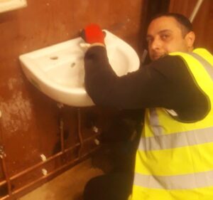 Owner in a yellow vest and gloves working on a sink